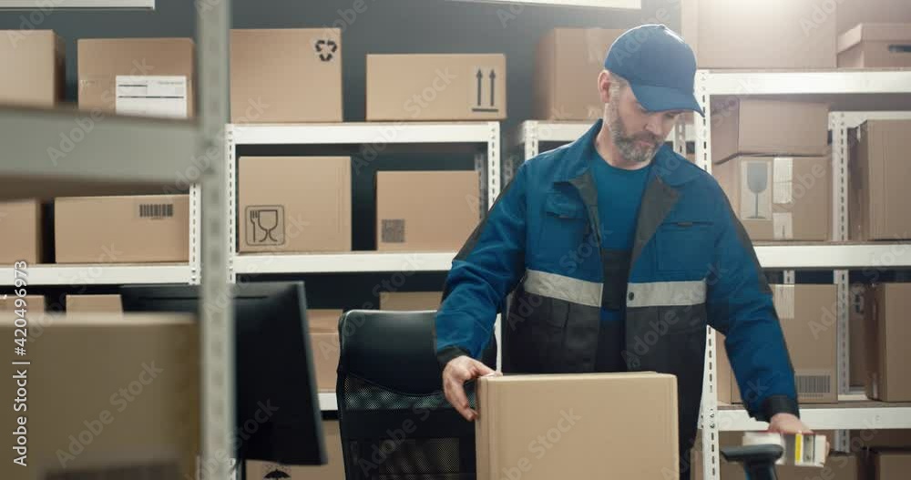 Portrait of diligent senior warehouse worker in uniform packing cardboard box with scotch tape and holding out parcel smiling pouring into the camera. Portrait of diligent senior warehouse worker in uniform packing cardboard box with scotch tape and holding out parcel smiling pouring into the camera.