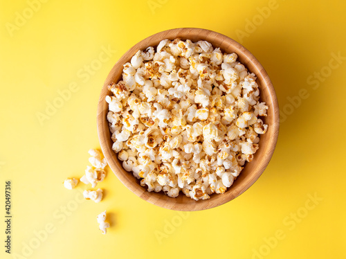 Wooden bowl with sweet popcorn on a bright yellow background. view from above