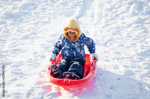 Cute boy child happily riding downhill on a toboggan sled