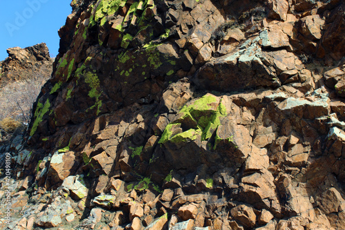 Weathered Lichen Covered Sheer Rock on Top of Cliff against Blue Sky 