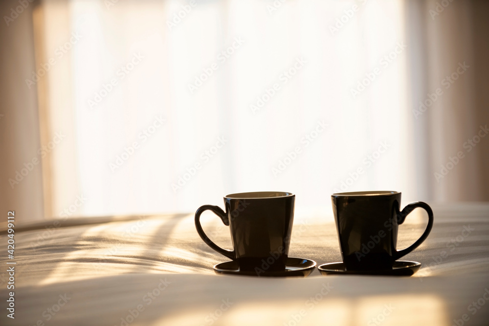 Two coffee mugs are placed on the bed. With the soft light of the morning near the window. Two coffee mugs are placed on the bed. With the soft light of the morning near the window.