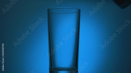 Transparent glass on a blue background with pouring water photo
