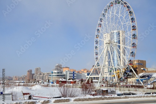 Ferris wheel with flags in Kazan near aquapark slides. Winter blue sky