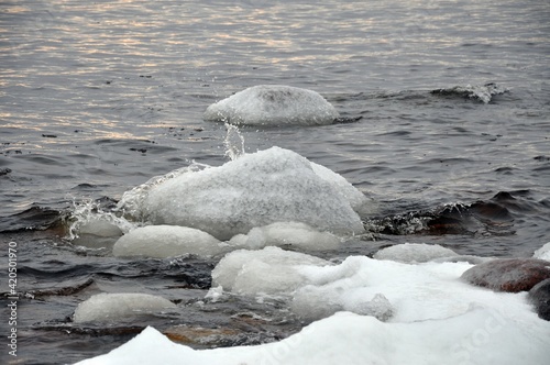 Frozen stones with ice. ice glaze Waves in a bay lake or sea. near shore. Sunset