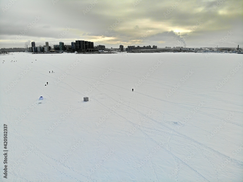 Fishermen fishing on ice in winter near the city. High-rise buildings background