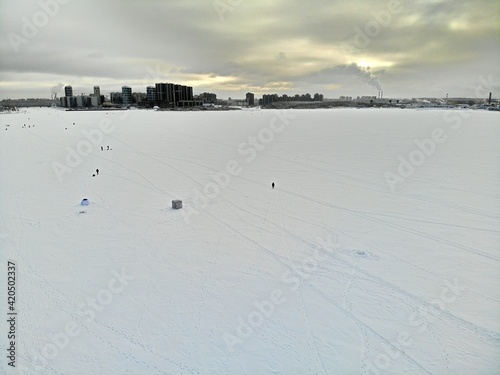 Fishermen fishing on ice in winter near the city. High-rise buildings background