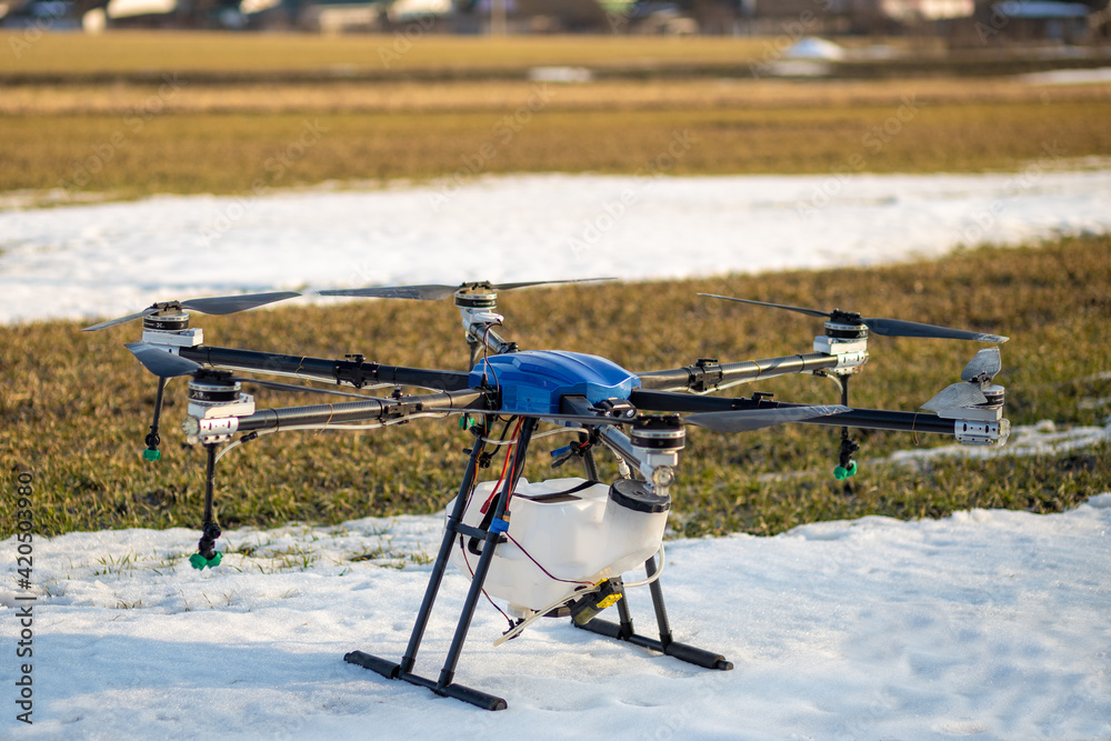 A beautiful blue agrodron stands on the field. Wheat grows. The snow has not melted yet. Agrodrons are ready to spray fertilizer. A beautiful blue agrodron stands on the field. Wheat grows. The snow has not melted yet. Agrodrons are ready to spray fertilizer.
