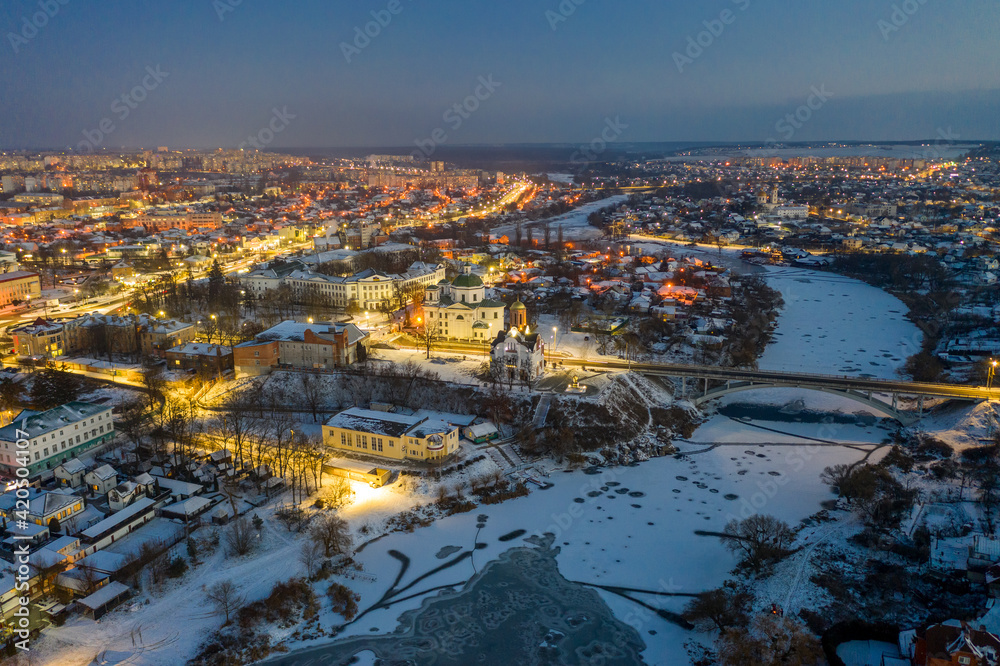 Beautiful evening top view of the city. Evening, night illumination in the city. Winter city in the snow. The river is covered with ice.