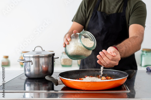 Cook throwing rice into the pan to prepare a spanish paella