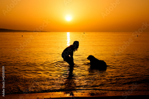 Tranquil scene with the silhouette of a woman and her dog having bathe in the sea during beautiful sunrise