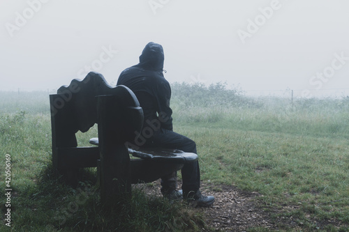 A man sitting on a bench on a moody foggy day in the countryside photo