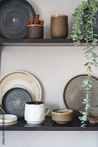 Stylish open space shelves with authentic handmade ceramic dishes, plants and plates. Design interior of cozy kitchen