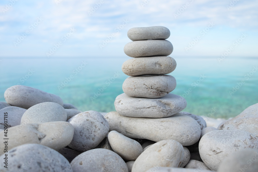 Flat rocks stacked on top of each other standing vertically on the beach, blue water and sky out of focus in the background, soft light. Balance, harmony, relaxation and peace concept. Space for copy. Flat rocks stacked on top of each other standing vertically on the beach, blue water and sky out of focus in the background, soft light. Balance, harmony, relaxation and peace concept. Space for copy.