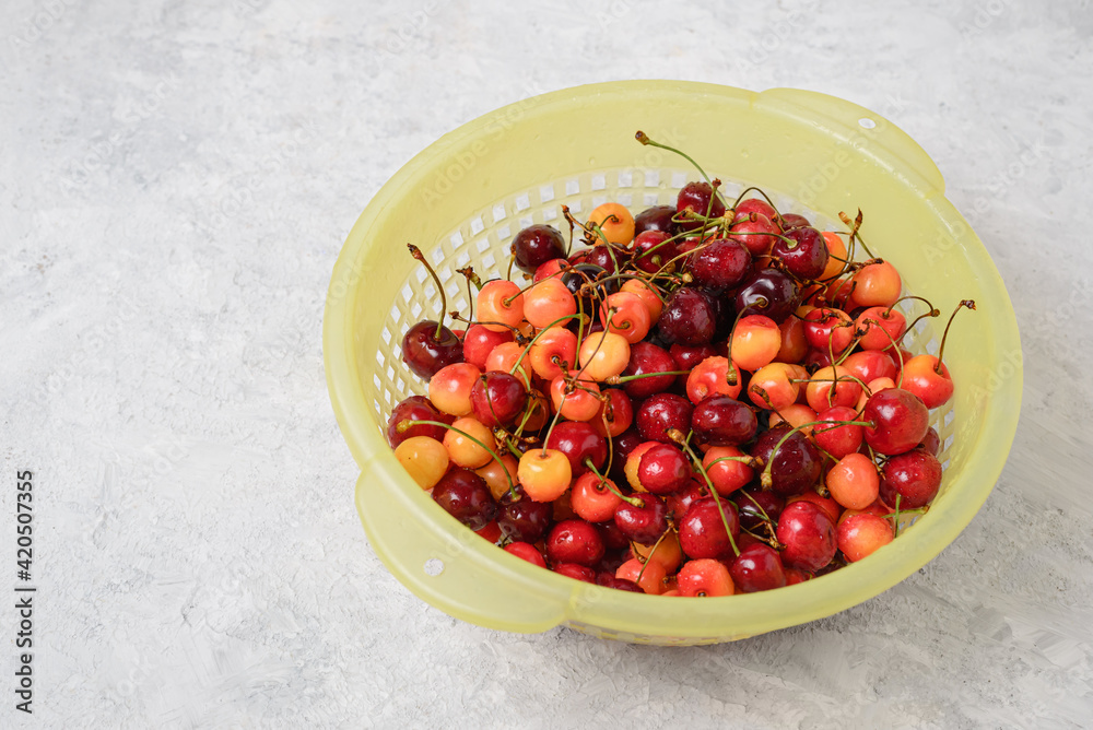 Red and yellow cherry berries in a yellow basket on a light textured background with copy space Red and yellow cherry berries in a yellow basket on a light textured background with copy space