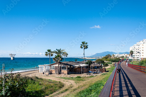 Panoramic sunny view of the sea coast, in the center on the beach there is an abandoned bar with palm trees, on the right there is a wooden pedestrian path that leads the city 