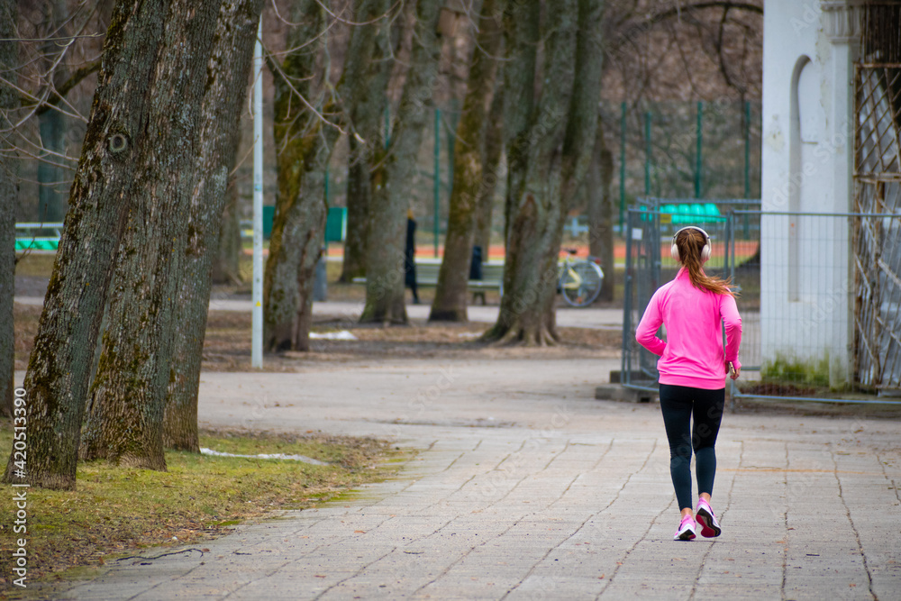 Blond girl running or jogging alone with headphones or headset in the park in the city