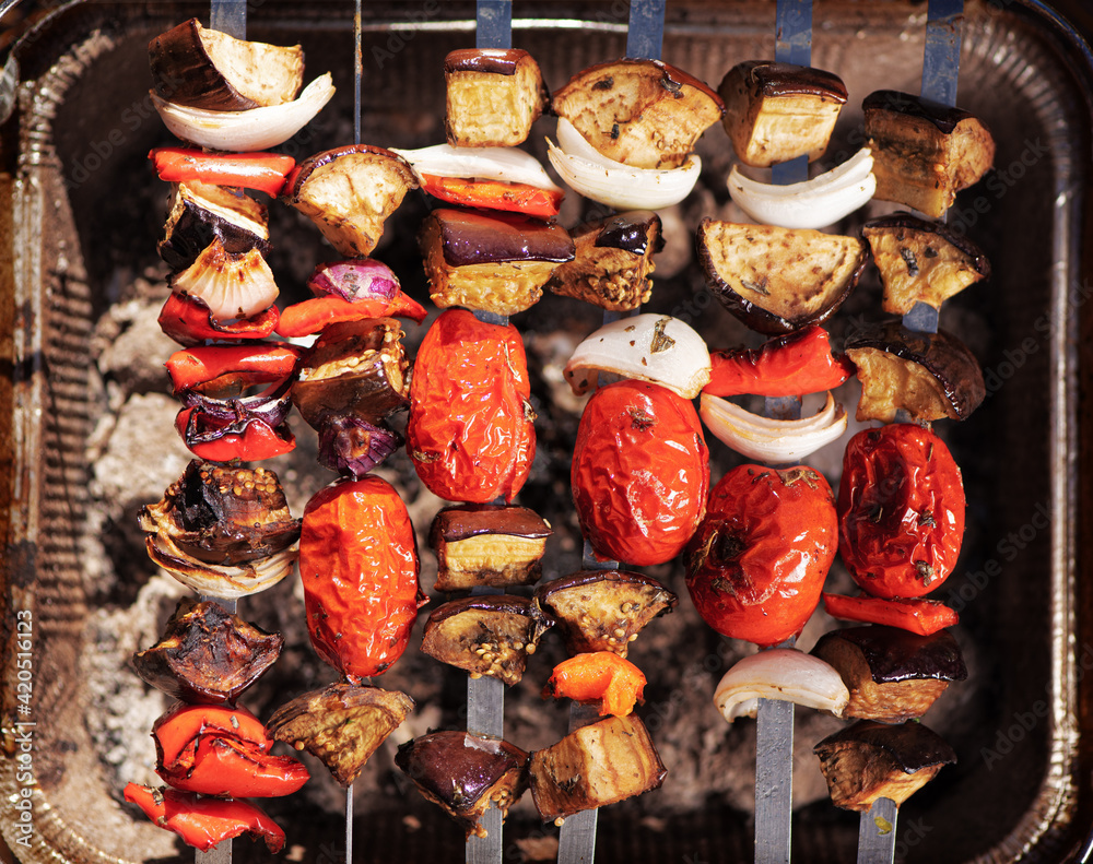 Cooking vegetables on grill outdoors. Grilled veggie skewers. Barbecue and picnic season concept. Top view.
