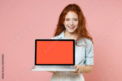 Young fun happy student businesswoman redhead freelancer woman 20s wear blue shirt hold laptop pc computer with blank screen workspace area gesture isolated on pastel pink background studio portrait. © ViDi Studio