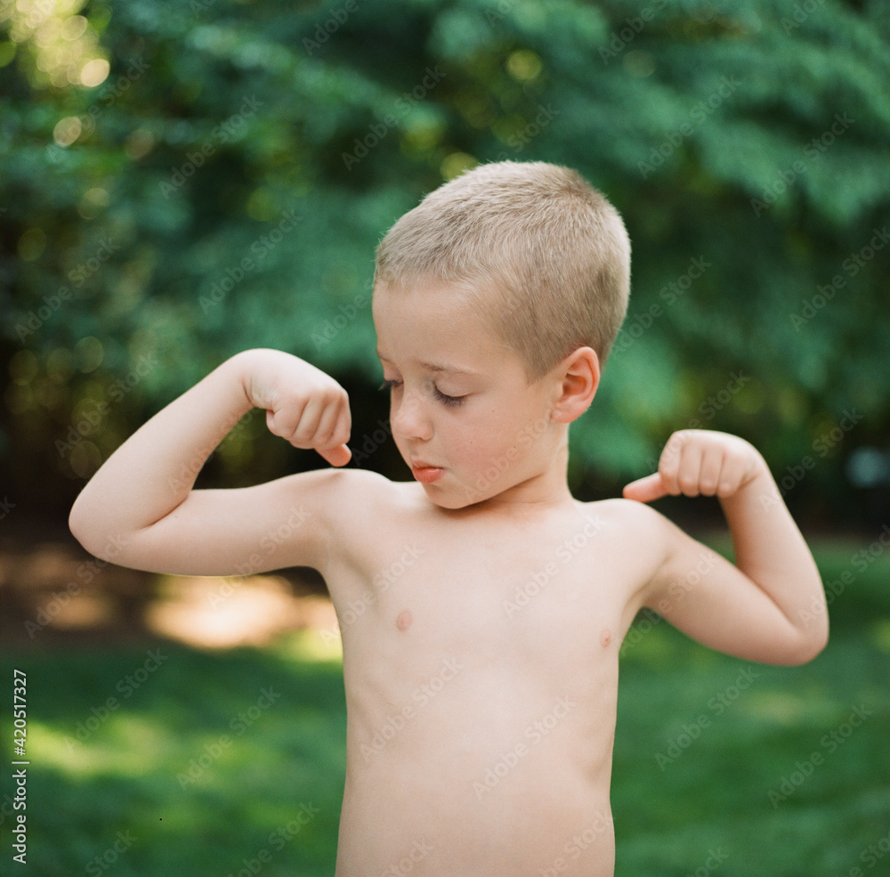 Cute young boy with no shirt pretending to flex his arm muscles Stock