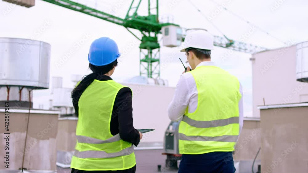 Charismatic lady assistant and the businessman on the roof top of construction site discussing about the plan of con they using a digital tablet man take the radio telecommunications to speak with
