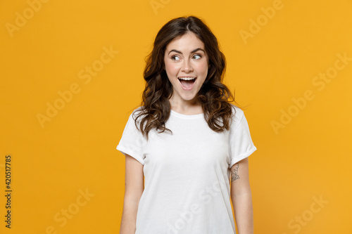 Young surprised shocked excited impressed amazed fun eueropean caucasian student woman 20s wearing white basic casual t-shirt looking aside isolated on yellow orange color background studio portrait.