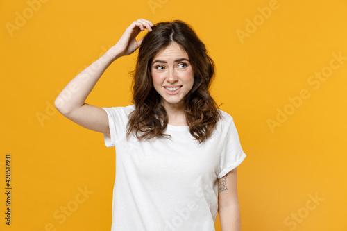 Young pensive thoughtful overthink mistaken troubled eueropean caucasian student woman 20s in white basic casual tshirt look aside sctratch head put hand isolated on yellow background studio portrait
