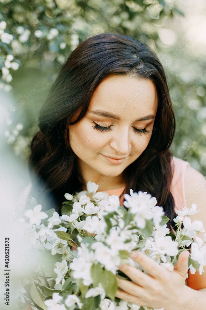 Gentle beautiful young happy brunette woman in a blue dress with a straw hat smiling relaxing enjoying a walk in the park in spring blooming apple trees outdoors, selective focus Gentle beautiful young happy brunette woman in a blue dress with a straw hat smiling relaxing enjoying a walk in the park in spring blooming apple trees outdoors, selective focus
