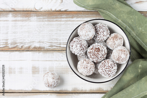 Coconut energy balls in a white cup on a light wooden background. Top view. photo