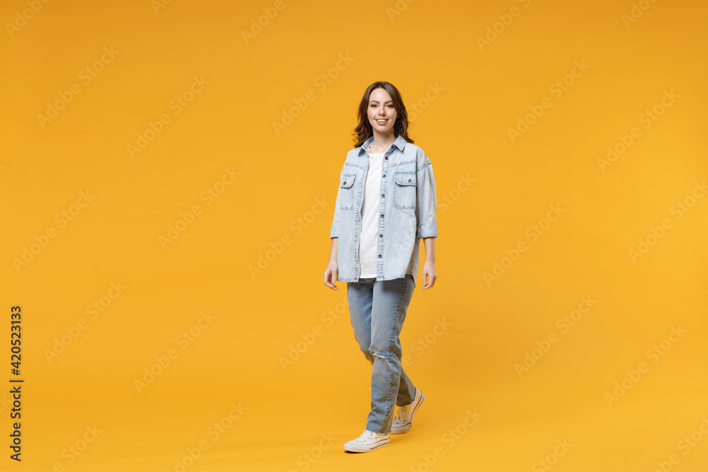 Full length of young caucasian smiling happy confident european cute woman 20s wearing stylish casual denim shirt white t-shirt walking going look camera isolated on yellow background studio portrait - obrazy, fototapety, plakaty 