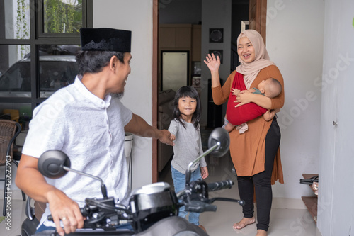 muslim man going by motorcycle scooter leaving his family behind at home. concept of asian family travelling photo