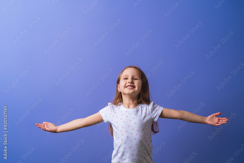 little girl of 5 years old with blonde hair in a T-shirt with colored polka dots spreads her arms to the side and smiles happily on a purple background. Close-up little girl of 5 years old with blonde hair in a T-shirt with colored polka dots spreads her arms to the side and smiles happily on a purple background. Close-up