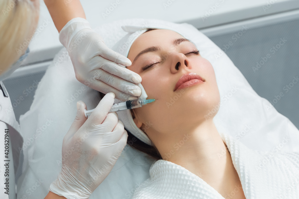 The doctor cosmetologist makes the rejuvenating facial injections procedure for tightening and smoothing wrinkles on the face skin of a beautiful, young woman in a beauty salon. Cosmetology, skincare