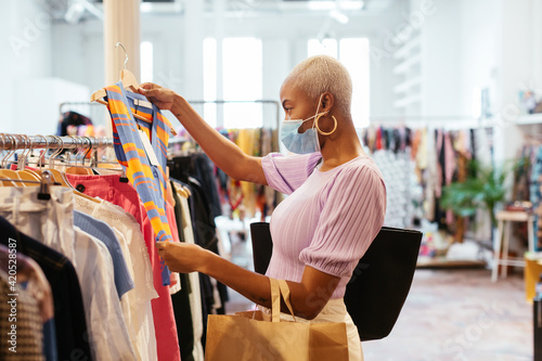 Black woman in mask choosing clothes in shop photo