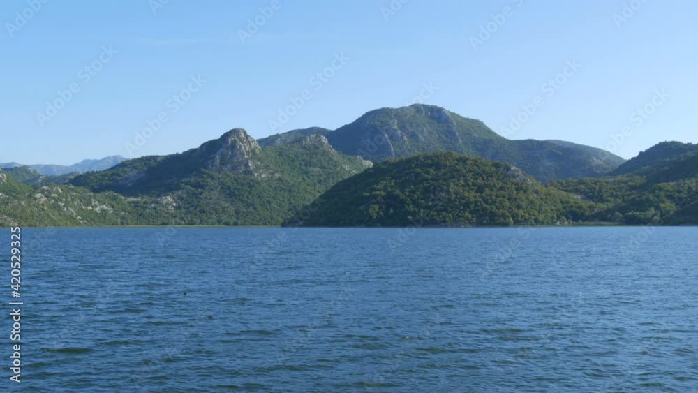 Blue river flowing through green valley toward distant mountains. Bends and curves of Crnojevica river in national park of Montenegro, meandering through the marsh among hills on way to lake Skadar Blue river flowing through green valley toward distant mountains. Bends and curves of Crnojevica river in national park of Montenegro, meandering through the marsh among hills on way to lake Skadar
