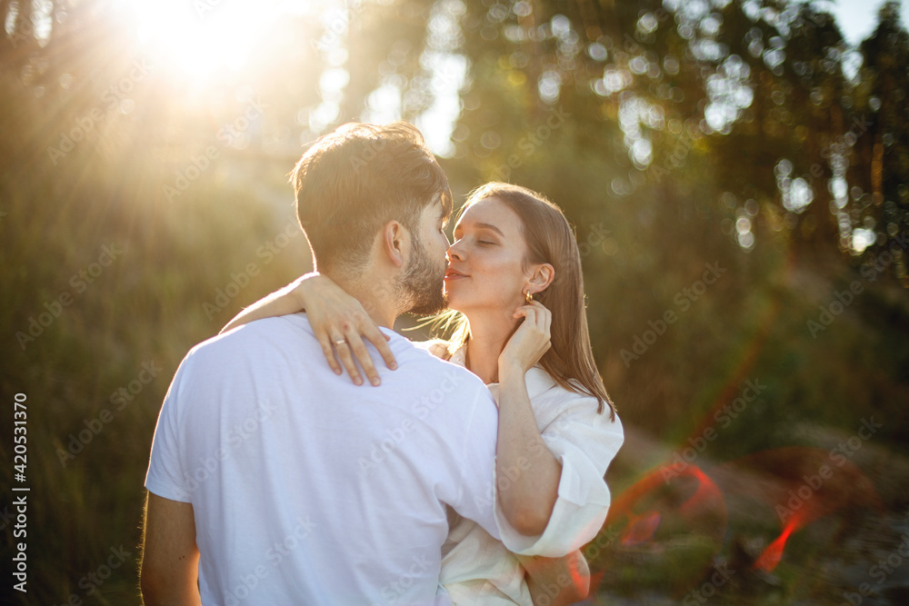 young bearded man gently kisses a young woman in white clothes in a park or forest at sunset. couple in love romantic relationship. love story young bearded man gently kisses a young woman in white clothes in a park or forest at sunset. couple in love romantic relationship. love story