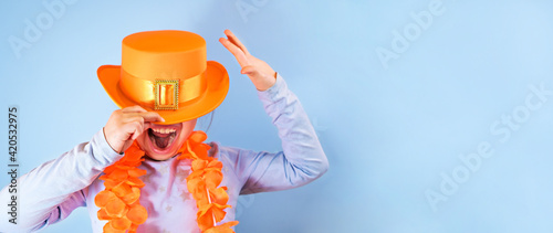 King's Day in Holland in the spring. Traditional festival on April 27 in the Netherlands. Little girl in a festive orange hat on a blue background eats colored donuts. Banner, long format. Copy space