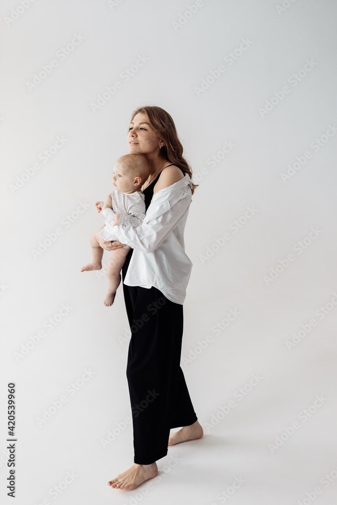 A gorgeous successful woman hugs her lovely baby tightly. A young mother and a lovely daughter are looking to the side with interest, smiling. Happy family concept A gorgeous successful woman hugs her lovely baby tightly. A young mother and a lovely daughter are looking to the side with interest, smiling. Happy family concept