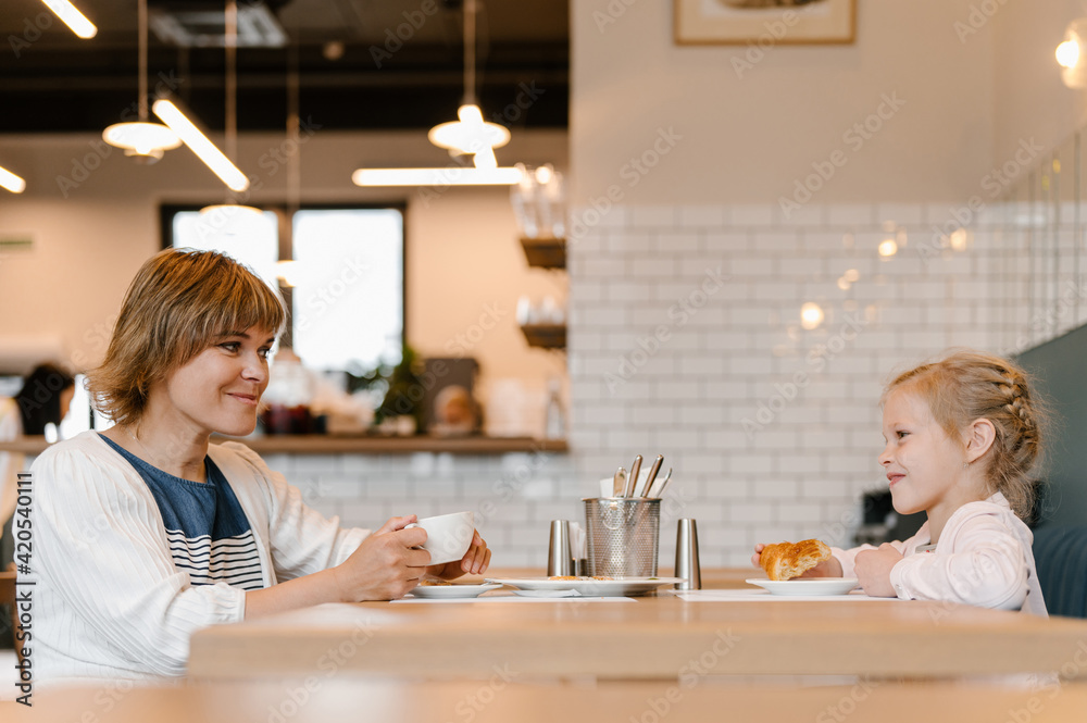 Content mother and daughter enjoying breakfast in cafeteria Content mother and daughter enjoying breakfast in cafeteria