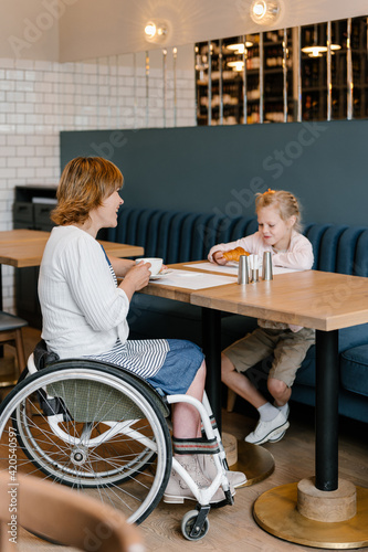 Cheerful mother using wheelchair with daughter in cafe