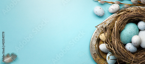 Happy Easter concept. Frame of Easter eggs and spring flowers on blue background. Flat lay, top view, copy space.