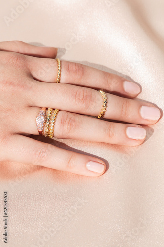 Woman wearing multiple rings on her finger, silky pink background