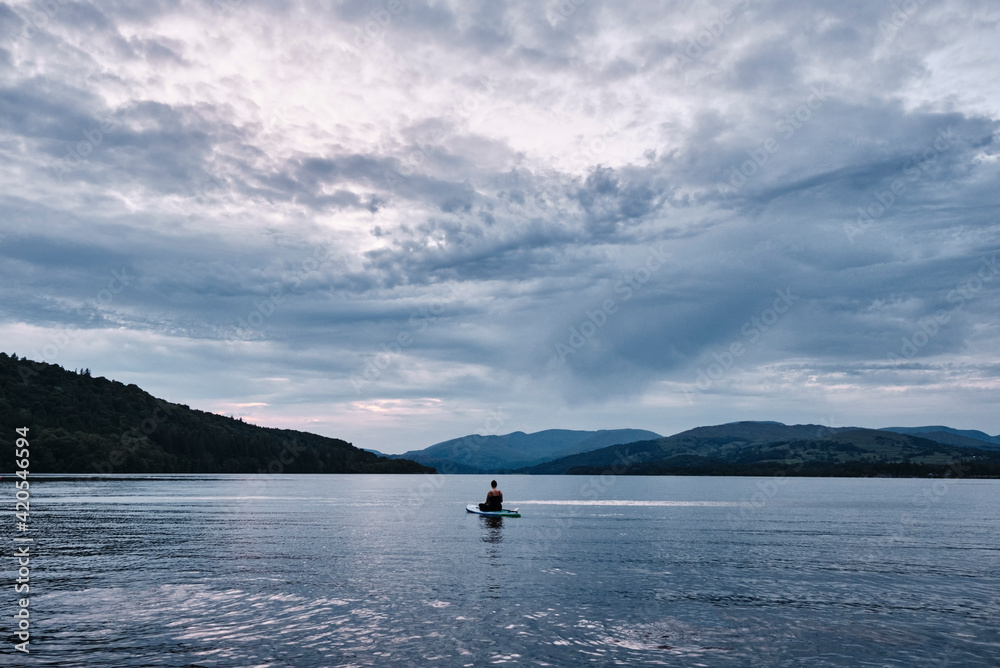 Female paddle boarding on Lake Windermere at sunset. Lake District, Cumbria, UK. Female paddle boarding on Lake Windermere at sunset. Lake District, Cumbria, UK.