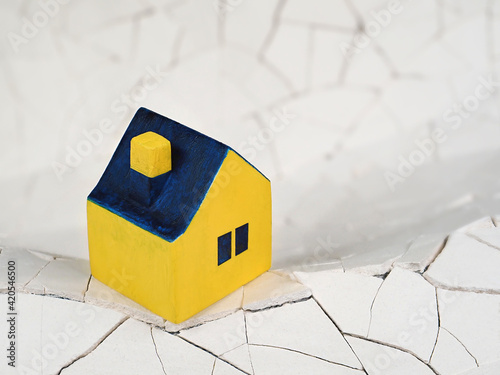 Miniature yellow toy house unstable stands on cracked ground, symbol photo