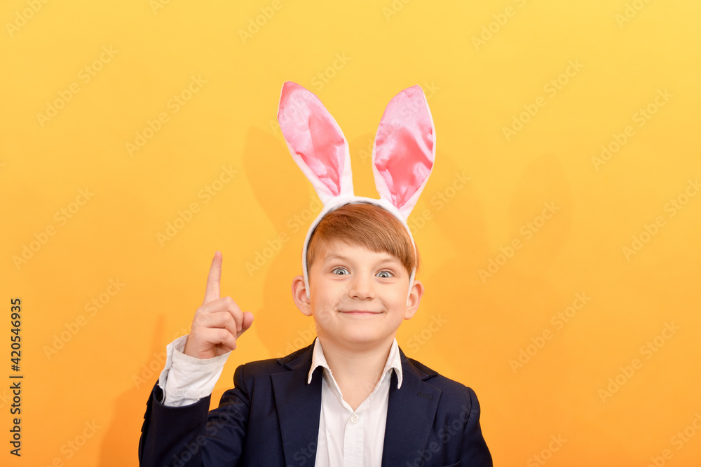 A boy with rabbit ears raised his index finger to the top on a yellow background.