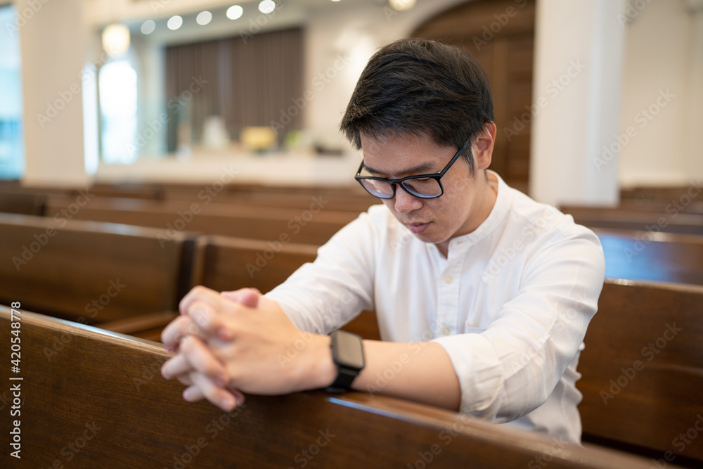 A man praying on a bench in a Christian church.