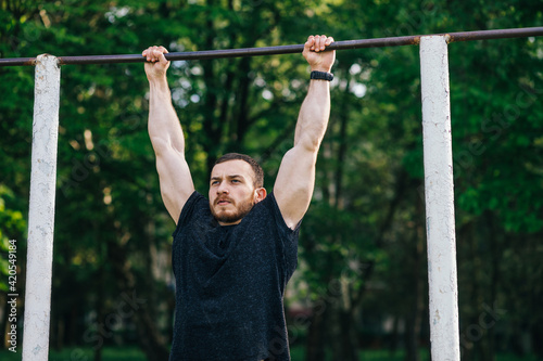 Strong muscular bearded man doing push-ups on bars in outdoor st