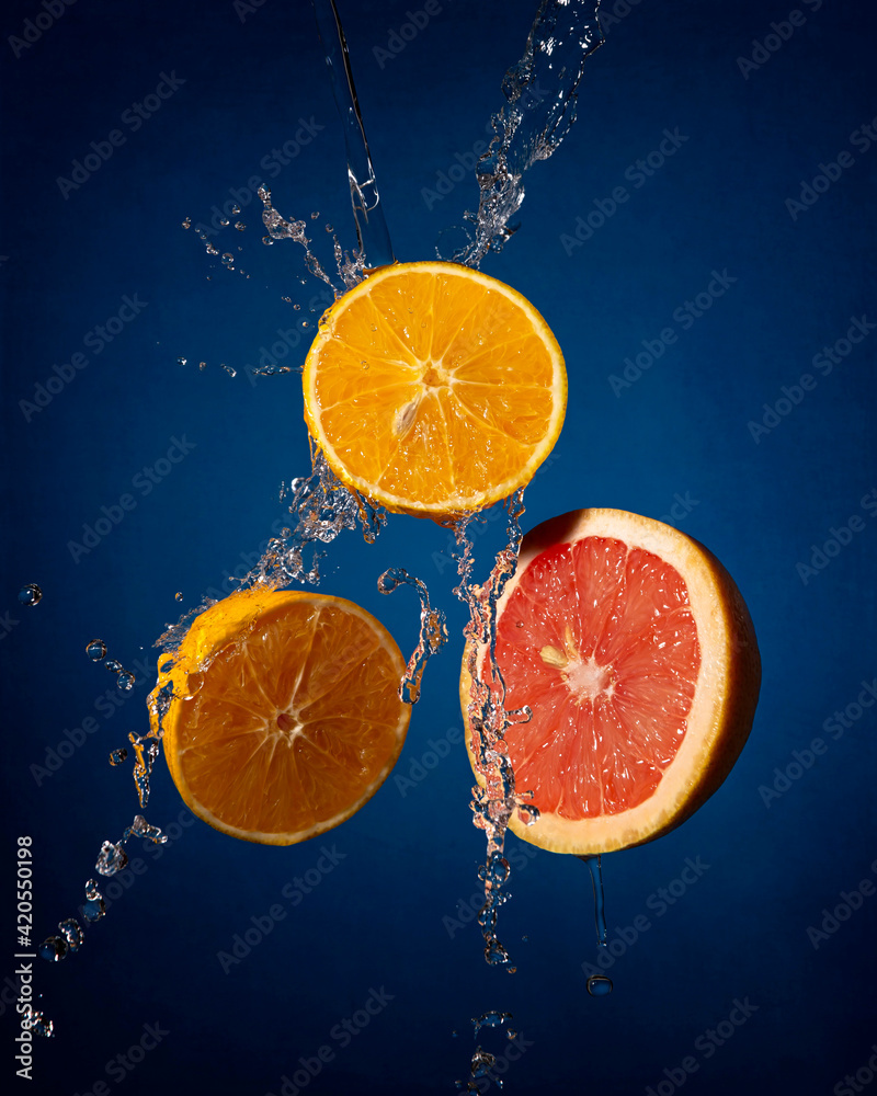 creative composition image of levitating orange and grapefruit slices with water splashing on dark blue background creative composition image of levitating orange and grapefruit slices with water splashing on dark blue background