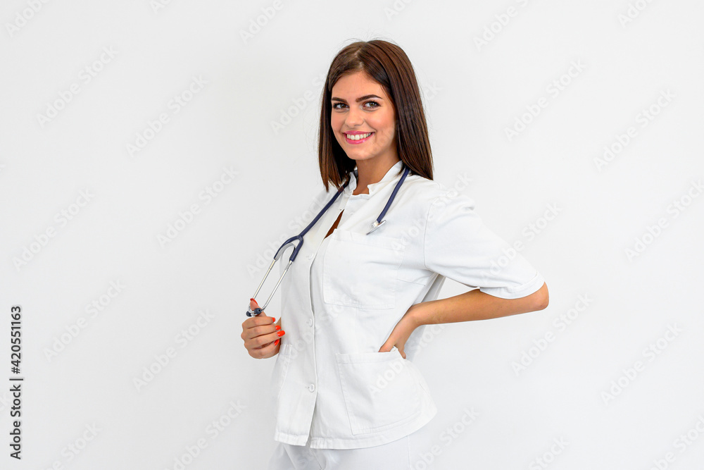 Charismatic young doctor posing. Brunette holding stethoscope around neck. She is wearing uniform. White background. Charismatic young doctor posing. Brunette holding stethoscope around neck. She is wearing uniform. White background.