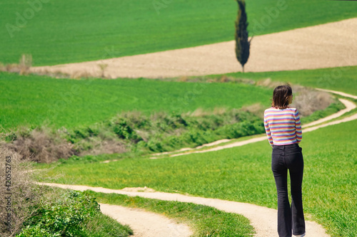 Young short hair brunette woman seen from behind walking on a path in the green field