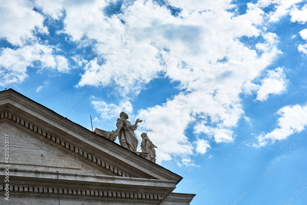 Obraz premium A view of sculptures on top of the Tuscan Colonnades and blue cloudy sky at St. Peter's Square in the Vatican city in Rome, Italy.